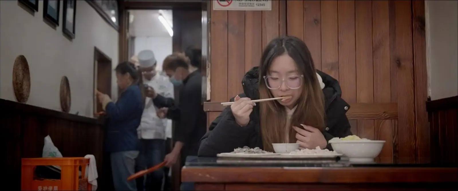 Film still: a woman eating noodles at a Beijing restaurant