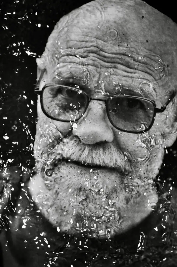 Black-and-white portrait of an older man behind water droplets